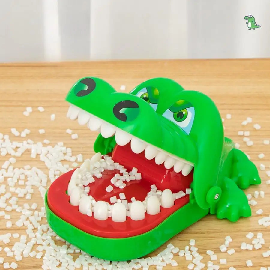 A bright green crocodile toy featuring a wide open mouth showing white teeth, resting on a wooden surface with small white sc