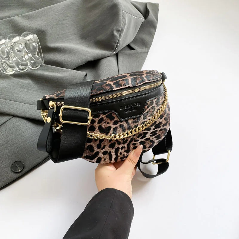 A hand holds a black and leopard print waist bag with gold hardware against a gray blazer.
