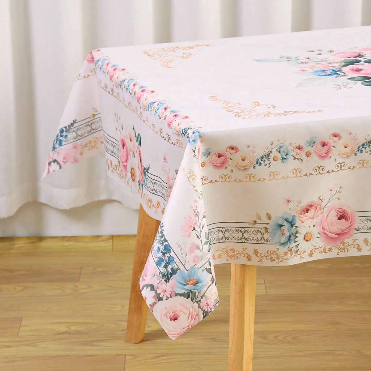 A white vintage floral tablecloth with pink, blue, and green accents is draped over a wooden table.