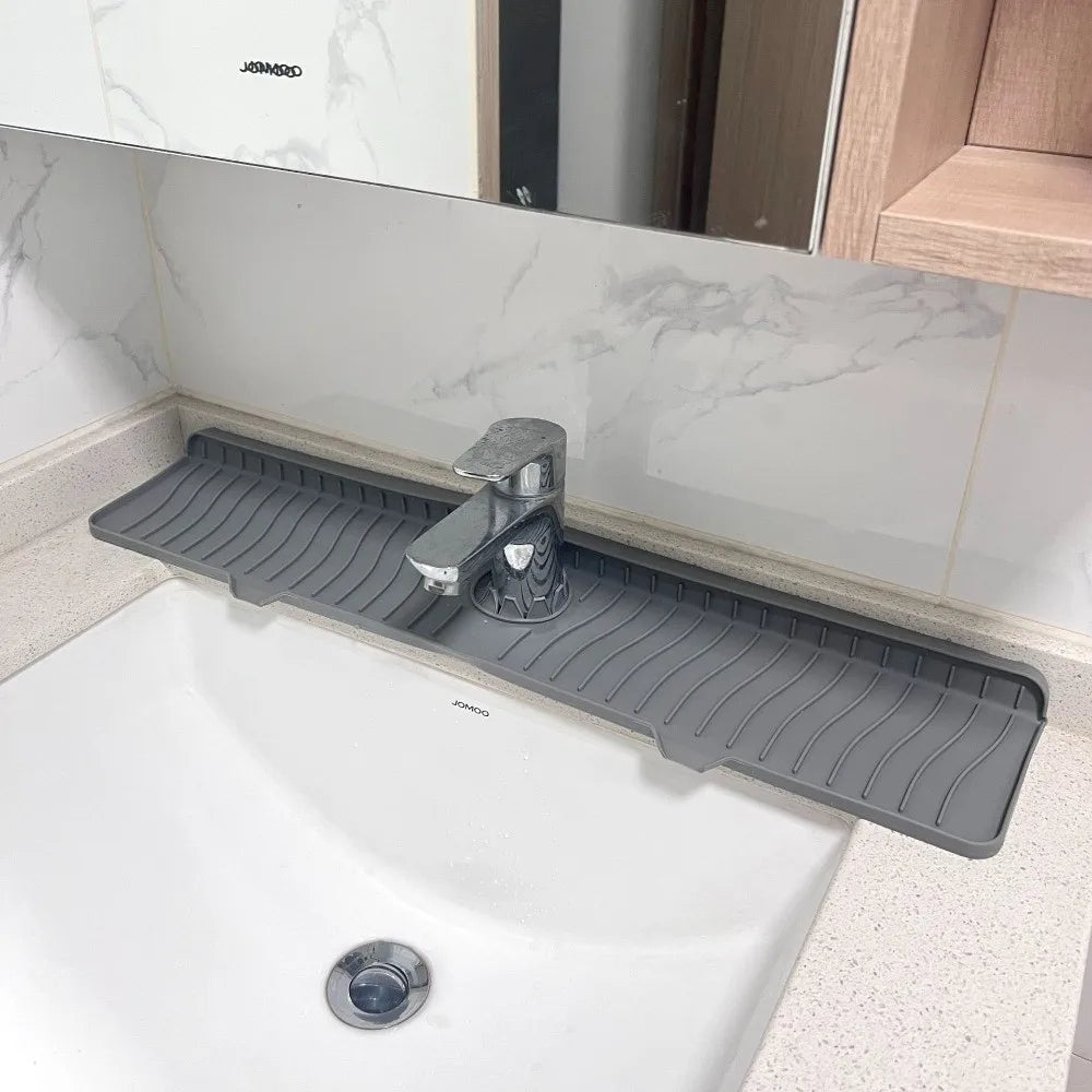 A black silicone faucet splash mat is placed on a white kitchen countertop next to a sink.