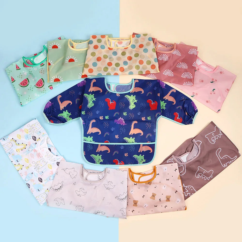 A collection of colorful waterproof long-sleeve baby bibs in various patterns and colors laid out on a light background.