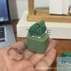 A hand holds a green fidget keychain with an LED light and sound feature.