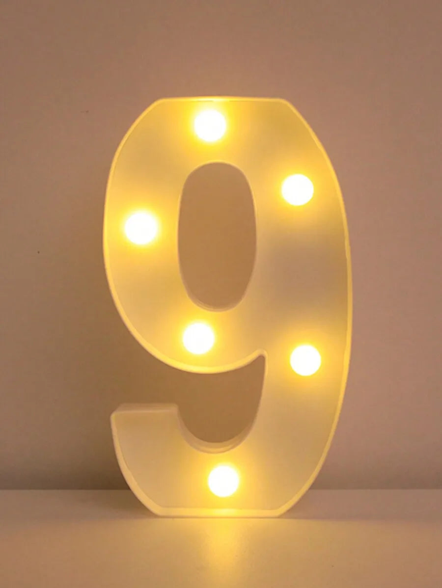 A glowing yellow LED letter night light shaped like the number 9, illuminating the surface it rests on.