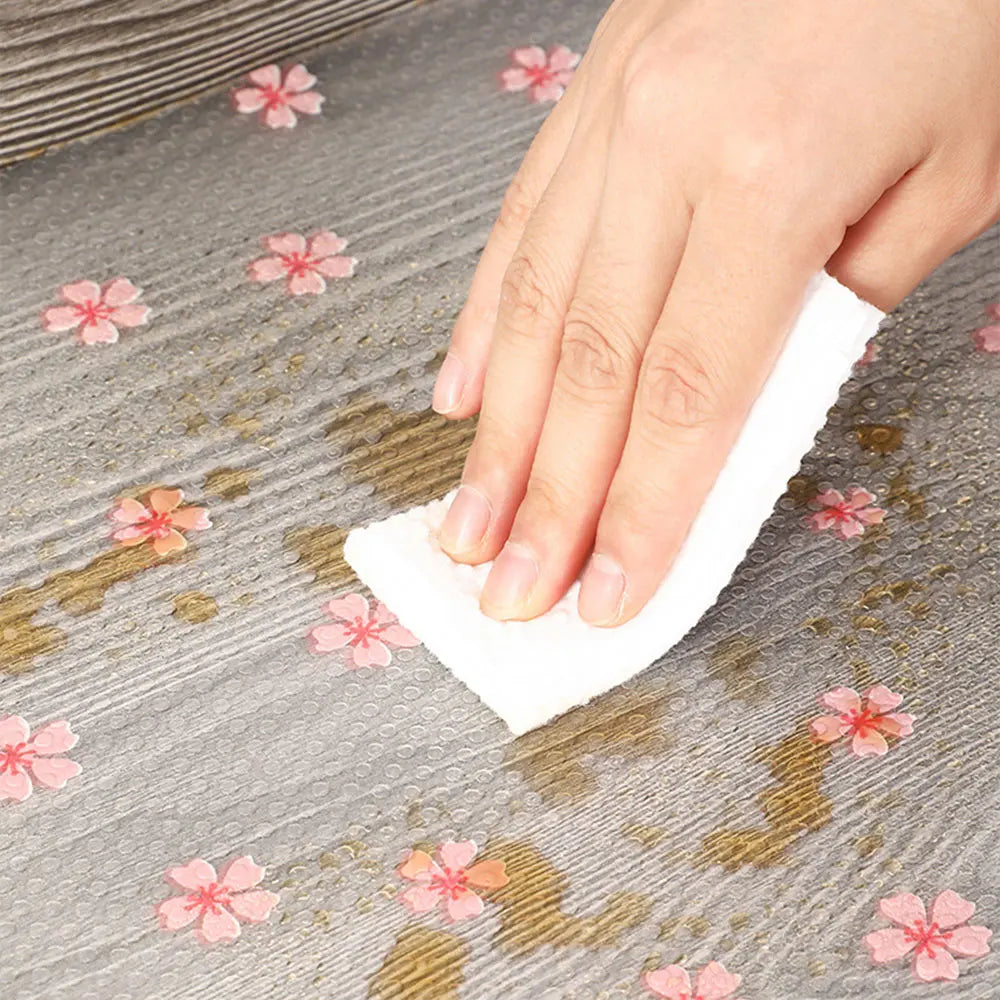 A hand is wiping a surface with a white cloth, which has light pink floral patterns on a gray background.
