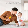A man is playing with a yellow cartoon animal rattle toy for a baby in a bright room.