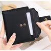 A hand holds a black compact RFID-blocking bi-fold wallet with gold accents, showing the interior card slot.