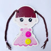 A pink wooden Montessori busy board featuring a girl's face and clothing with purple and yellow buttons.