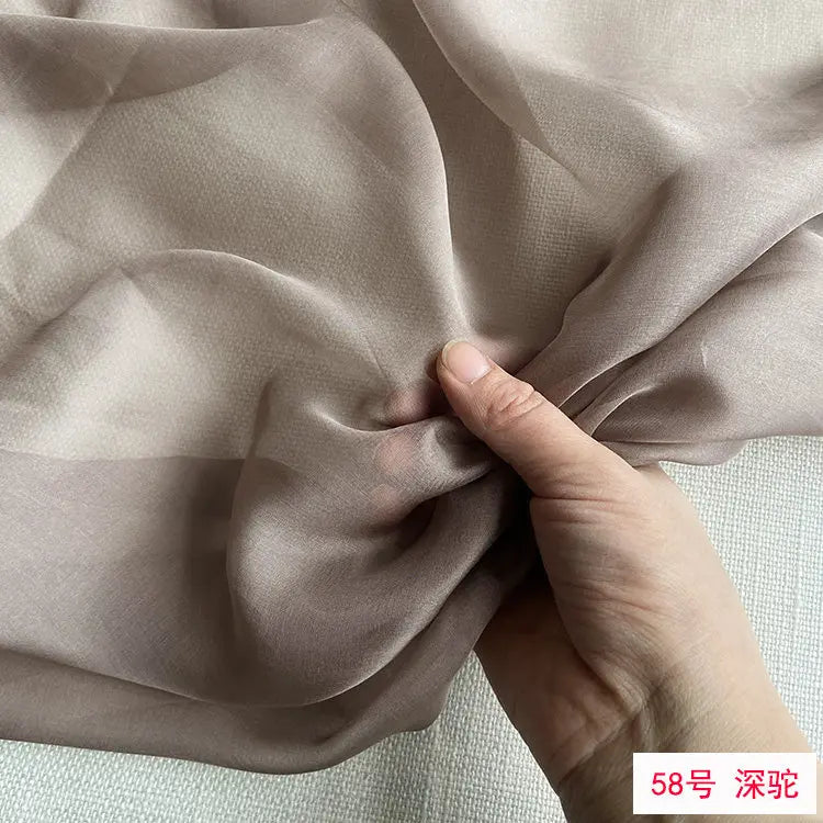 Close-up of beige silk chiffon fabric being gathered by a hand