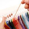 A hand is holding a set of twelve colored embroidery floss strands for a cross stitch kit.