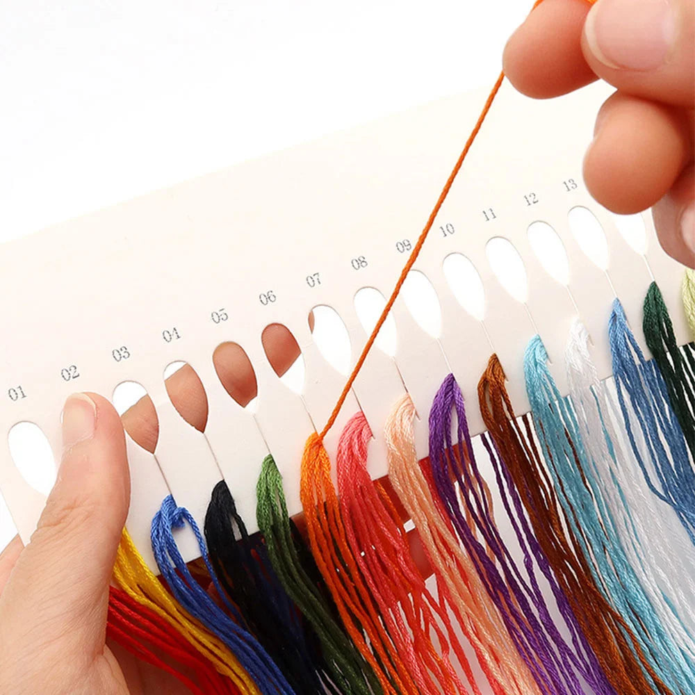 A hand is holding a set of twelve colored embroidery floss strands for a cross stitch kit.