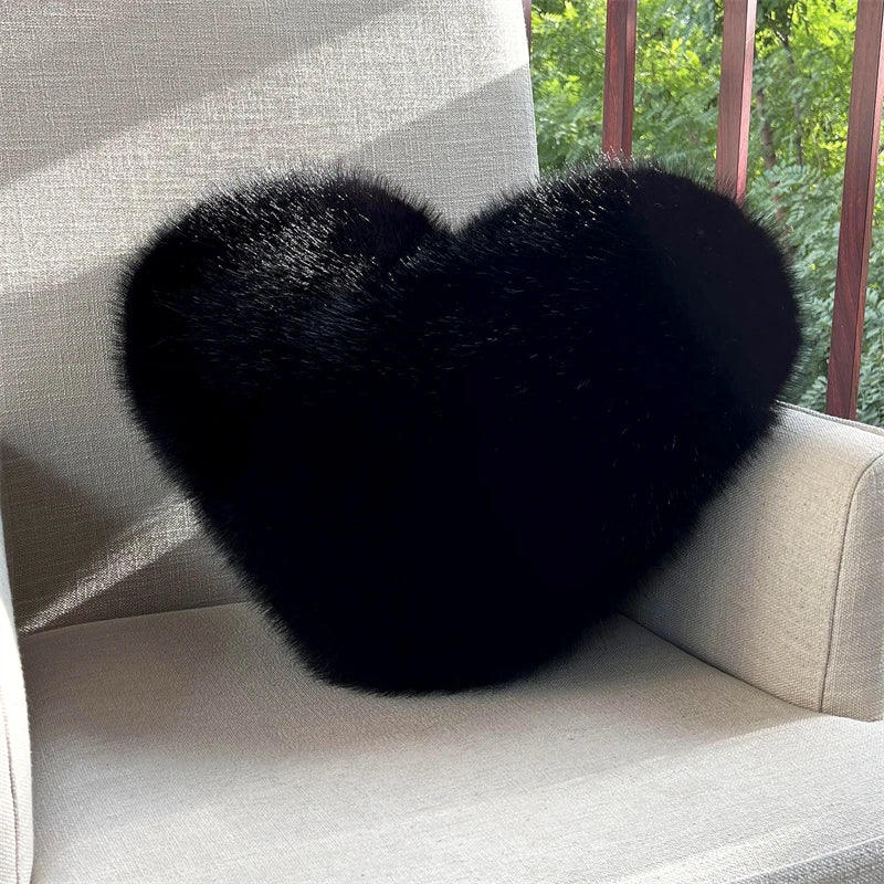 A black, heart-shaped plush throw pillow resting on a light-colored sofa.