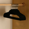 Black velvet non-slip hangers hanging from a wooden rod on a closet door.