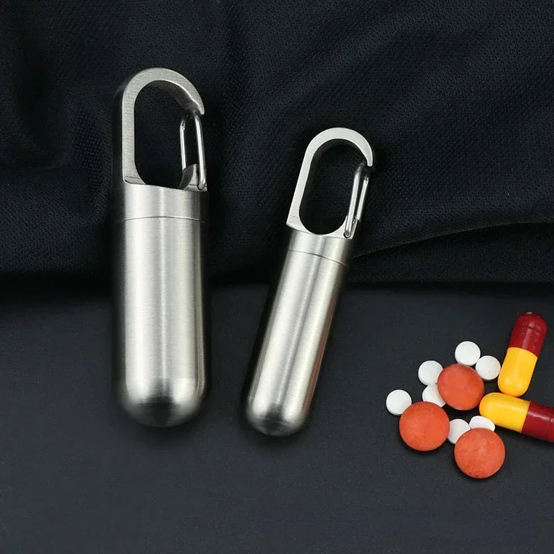 Stainless steel pill capsule with a keychain attached, shown against a dark background.