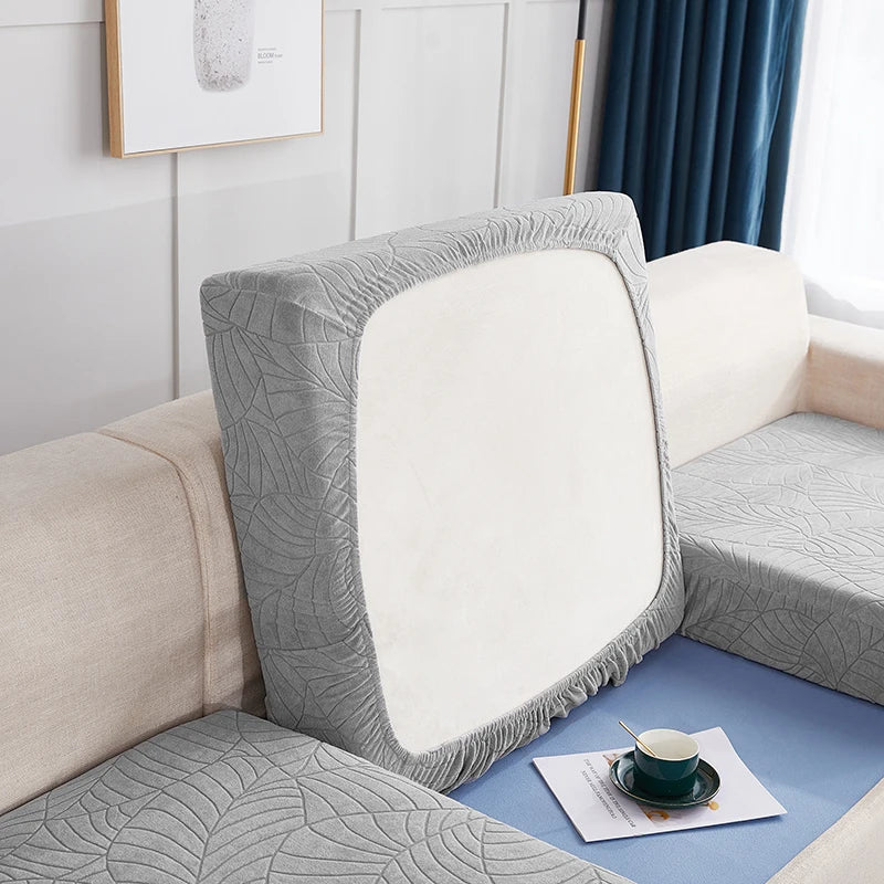 A close-up of a gray stretch jacquard sofa cover with an anti-slip backing and a white cushion on a light beige sofa.