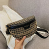 Schwarze und goldene Leopardenmuster-Crossbodytasche auf weißem Strick auf grauem Sofa.