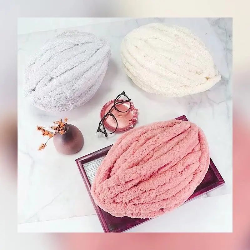 A pile of pink chenille yarn is displayed on a white marble surface with small accessories.