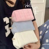 A hand holds a stack of four pink, blue, and white quilted portable makeup bags.