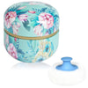 A round, light blue container with floral patterns and a gold rim, shown next to a white cosmetic puff.