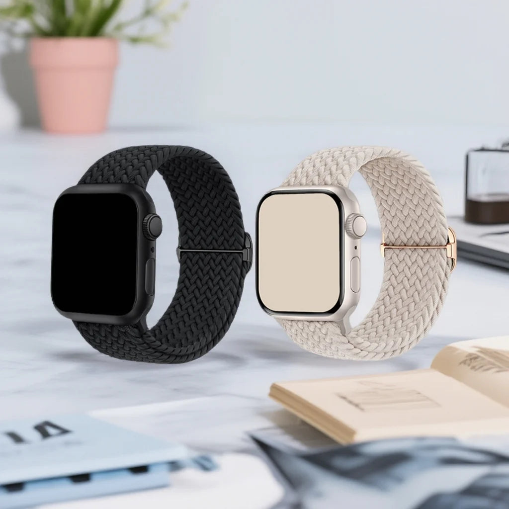 A black and beige braided nylon watch band is shown next to a square Apple Watch, resting on a light surface with some papers