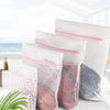 Several white mesh laundry bags filled with clothing are displayed on a white surface.