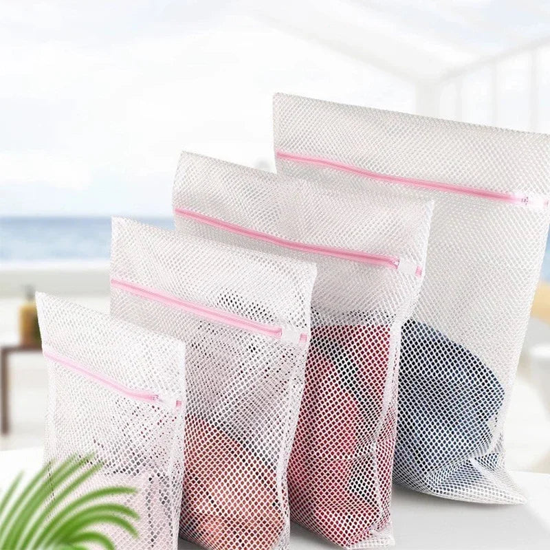 Several white mesh laundry bags filled with clothing are displayed on a white surface.