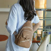 A person is holding a tan PU leather crossbody bag with a gold-toned adjustable strap.