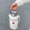 A hand is holding a white insulated stainless steel tumbler with a lid and straw on an asphalt surface.