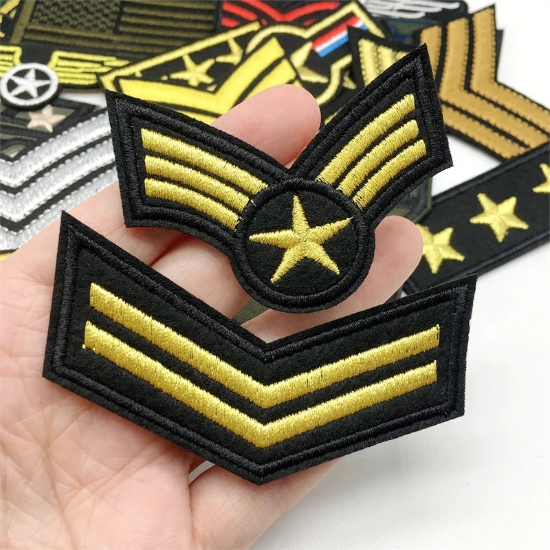 A hand holds a set of tactical embroidered patches featuring gold and black military style insignia.