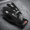 A pair of black full finger nylon riding gloves with anti-slip grips resting on a gray textured surface.