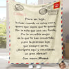 A beige flannel throw blanket with a personalized Spanish message and stamps, displayed on a light wooden surface.