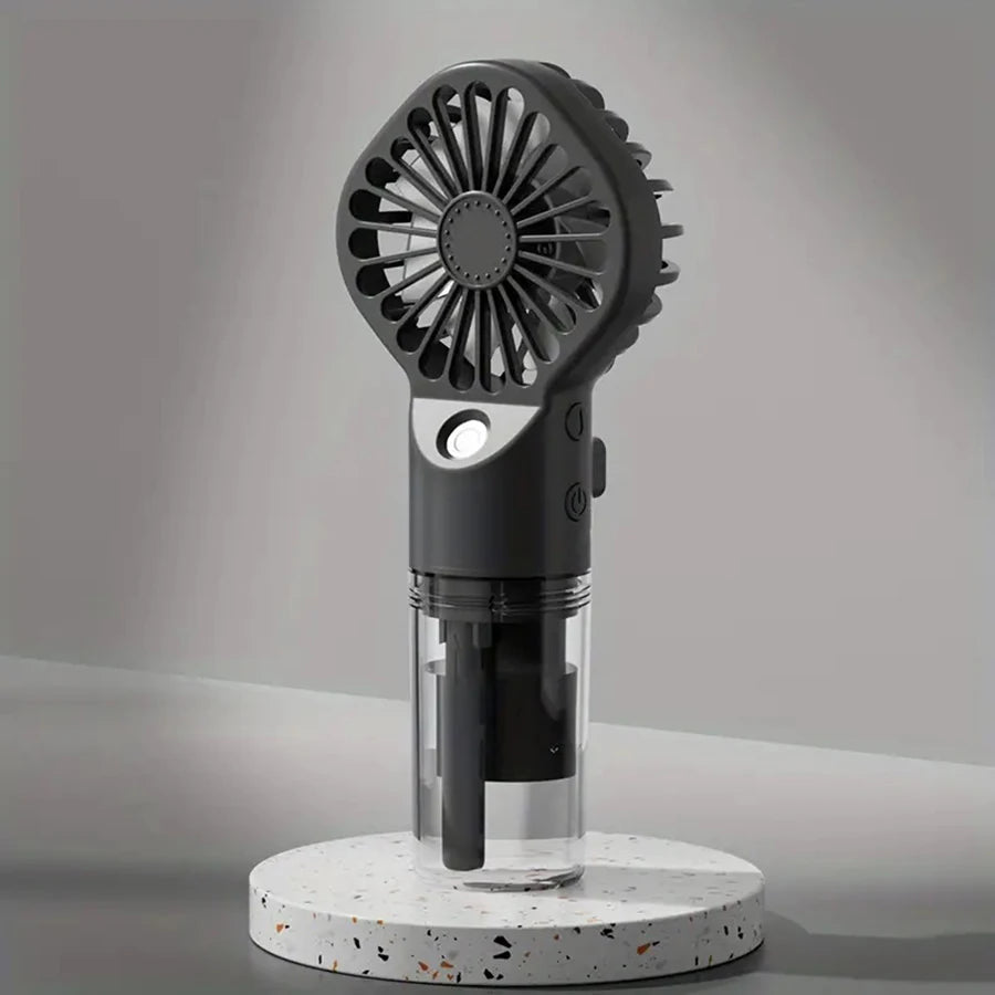 A black portable rechargeable handheld spray fan with a grille and clear cylindrical body sits on a white speckled platform.