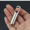 A hand holds a stainless steel waterproof pill capsule with a keychain attached.