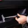 A hand is using a silver retractable car mirror and window cleaning wiper on a black vehicle interior.