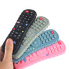 A hand holds a stack of silicone baby teether toys shaped like a TV remote in various colors.