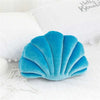 A teal velvet shell shaped decorative throw pillow resting on a white surface.