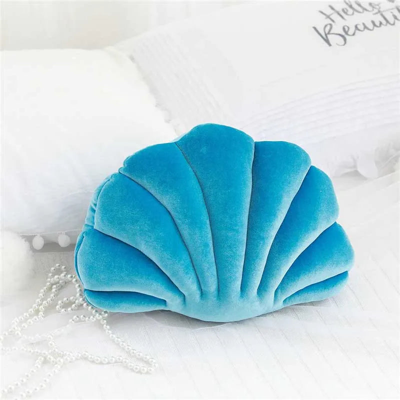 A teal velvet shell shaped decorative throw pillow resting on a white surface.