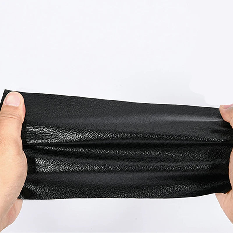 A hand is holding a black self-adhesive PU leather repair patch, showing its texture and thickness.