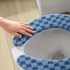 A hand is touching a blue and gray checkered plush cushion cover for a toilet seat.