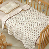 A white baby swaddle blanket with a bear print pattern is displayed on a wooden crib railing.