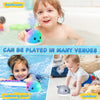 A baby is playing with an interactive light-up whale bath toy that sprays water in a swimming pool or outdoor setting.