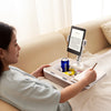A woman is using a 360° rotatable phone stand and lap desk to view content on a tablet while relaxing on a sofa.