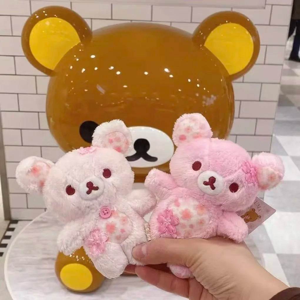 A pink cherry blossom plush bear is held next to a large golden bear toy.