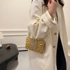 A woman wearing a cream-colored coat is holding a gold rhinestone evening clutch.