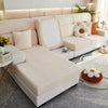 A modern, light beige sofa with a quilted slipcover and cream cushions is shown in a bright living room setting.