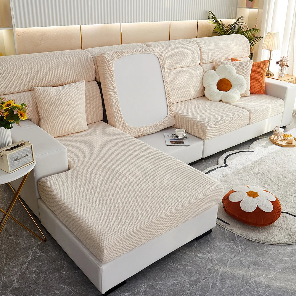 A modern, light beige sofa with a quilted slipcover and cream cushions is shown in a bright living room setting.