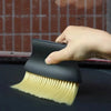A hand holds a black detailing brush set with soft yellow bristles against a dark surface.