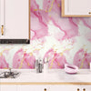 A kitchen backsplash featuring a pink and gold marble pattern wallpaper on the wall above a white countertop.