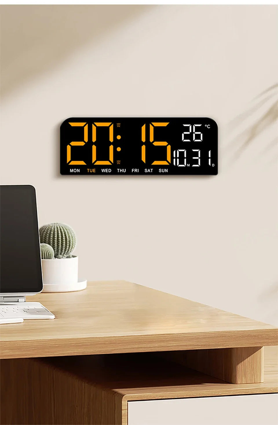 A black digital wall clock displaying the time 20:15 and a temperature of 26 degrees on a wooden desk.