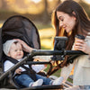 Eine Frau hält ein Baby in einem Fahrrad-Handyhalter mit verstecktem Tracker vor einem weichen Outdoor-Hintergrund.