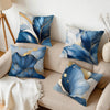 A collection of abstract leaf print cushions in shades of blue, white, and gold on a beige sofa.